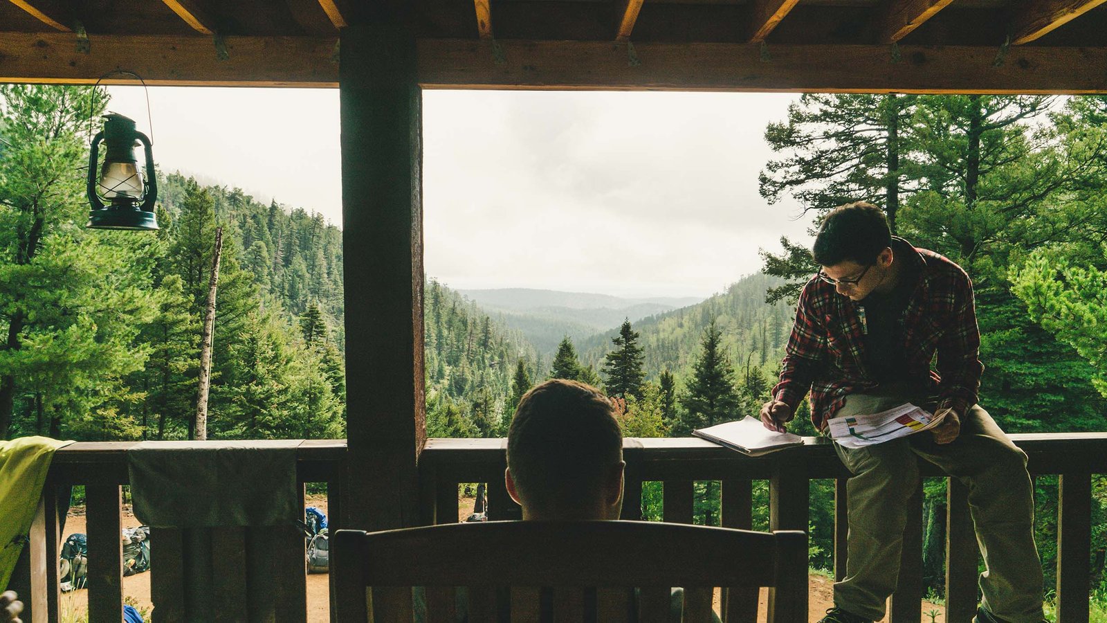 Two people working on a cabin porch overlooking the forest